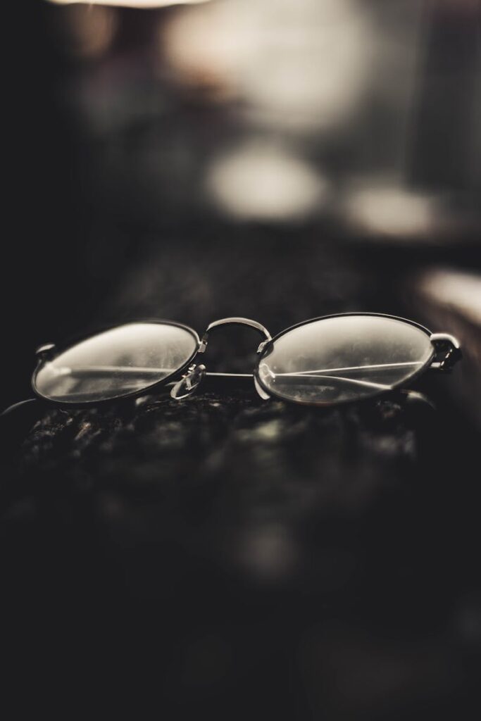 A pair of round eyeglasses resting on a textured dark surface, highlighted with bokeh effect.